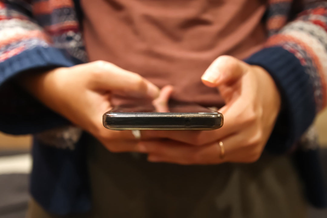 A close-up image of someone holding a phone with their hands, with both hands hovering over the screen showing they are engaged with it. 