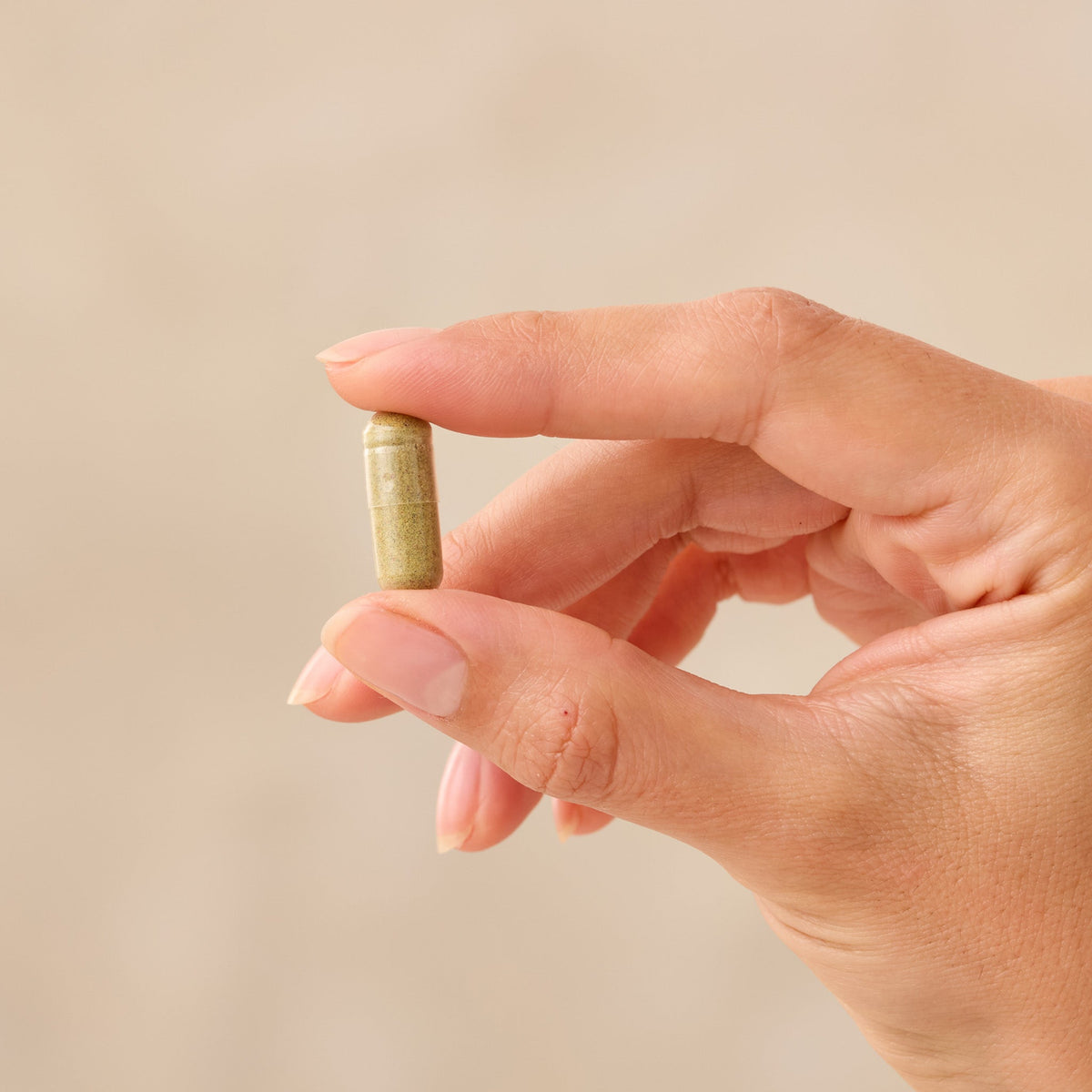Hand holding a small Juice Plus+ capsule against a beige background