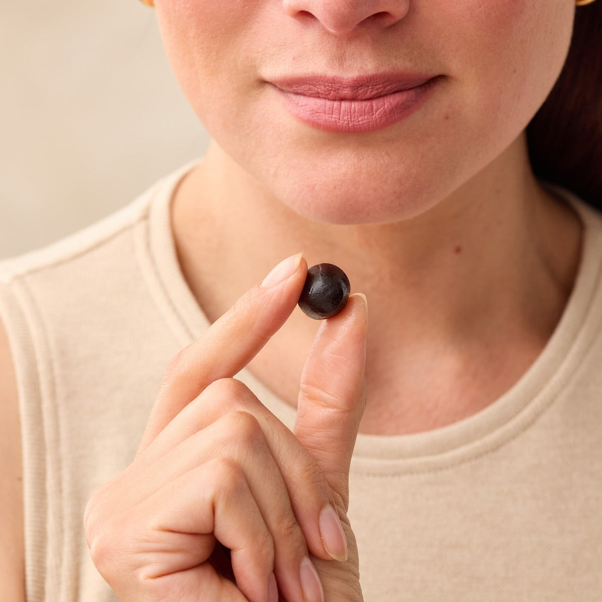 Person holding a Juice Plus+ chewable between their fingers against a neutral background