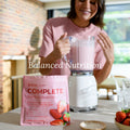 Woman preparing a shake with JuicePlus+ Complete Nutrition Shake Mix in a kitchen.