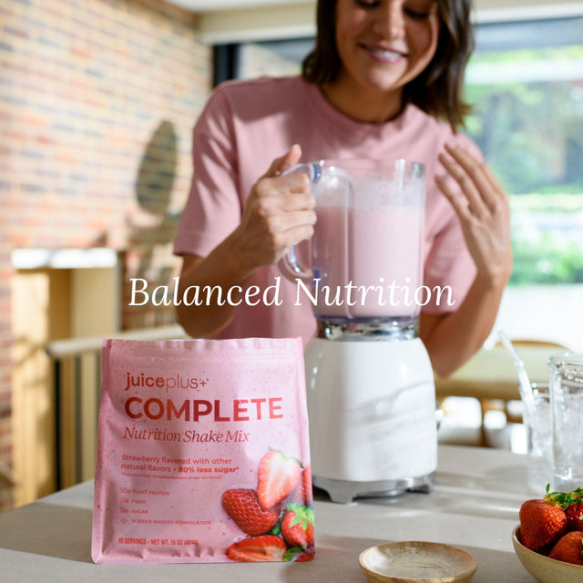 Woman preparing a shake with JuicePlus+ Complete Nutrition Shake Mix in a kitchen.
