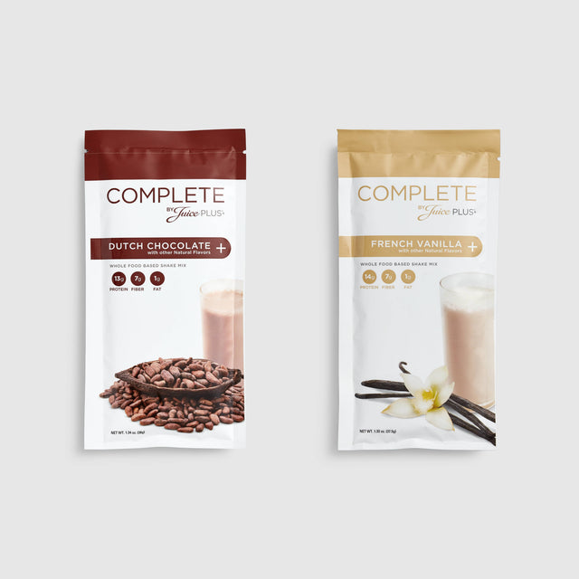 Two packages of Complete Food Variety Shakes, one with chocolate flavor and one with vanilla flavor. Each package has an image of ingredients like chocolate chips and vanilla pods.